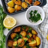 air fryer roasted potatoes with Greek seasonings in a bowl with sliced lemon and chopped parsley on the side