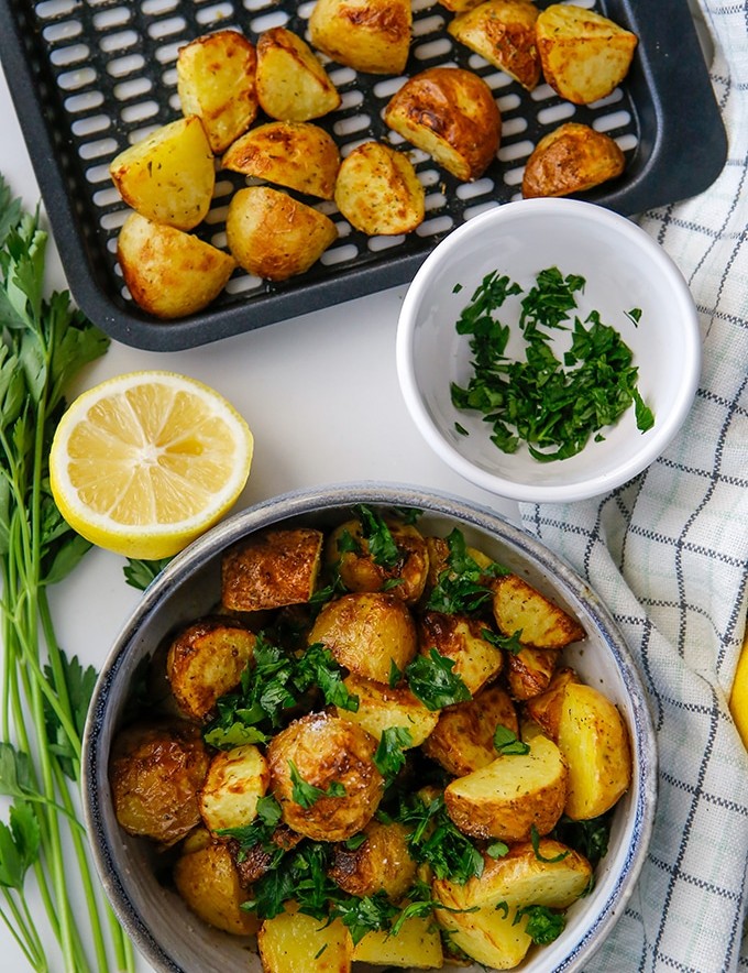 air fryer roasted potatoes with Greek seasonings in a bowl with sliced lemon and chopped parsley on the side