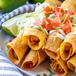 Instant Pot Chipotle Chicken Taquitos on a plate topped with sour cream and salsa and sliced limes on the side