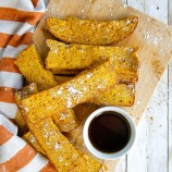 Air Fryer Pumpkin French Toast Sticks on a wooden board with syrup on the side