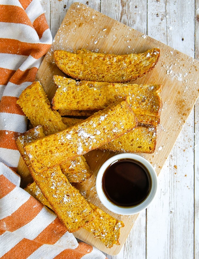 Air Fryer Pumpkin French Toast Sticks on a wooden board with syrup on the side