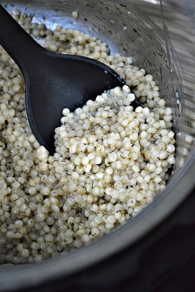 serving cooked Israeli couscous with a large plastic spoon from the pressure cooker
