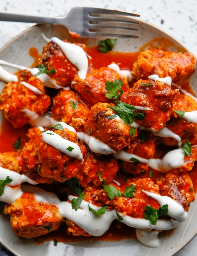 pressure cooker chicken meatballs with buffalo sauce, ranch dressing, and chopped parsley on a white plate