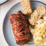 Air Fryer Bacon-Wrapped Pork Tenderloin in a serving plate with bread and potatoes on the side